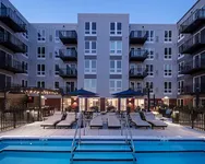 Modern apartment complex with a luxurious pool area at twilight, featuring comfortable lounge chairs and elegant balconies.