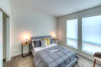 Inviting bedroom with modern décor, featuring a plush gray bedspread, stylish accent pillows, and warm lighting from sleek bedside tables.