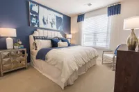 Elegant bedroom showcasing a plush bed with luxurious bedding, modern side table, and a large abstract artwork against a navy accent wall.