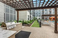 Luxurious outdoor apartment amenities featuring a stylish pergola, modern grill area, and inviting poolside loungers with vibrant orange cabanas.