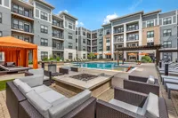 Modern apartment courtyard featuring luxurious poolside seating, vibrant orange cabanas, and a sparkling pool surrounded by stylish multi-story buildings.