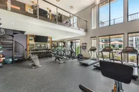 Spacious modern gym with floor-to-ceiling windows, state-of-the-art equipment, and a chic spiral staircase leading to a mezzanine level.