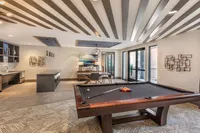 Elegant recreational room with a modern pool table, sleek bar area, and stylish decor with natural light streaming through large windows.
