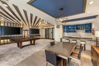 Modern entertainment room featuring a stylish billiard table, elegant bar area with stools, and contemporary shelving with unique decor accents.