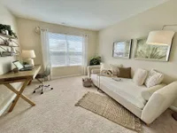 Elegant home office with natural lighting, featuring a cozy beige couch, plush pillows, and a wooden desk with decor accents.