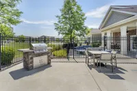 Charming outdoor patio with a modern grill, dining set, and lush garden view, perfect for entertaining.
