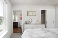 Bright and elegant bedroom with an en-suite bathroom, featuring modern decor and a spacious closet. Natural light floods the room through large windows, creating a serene and inviting atmosphere.