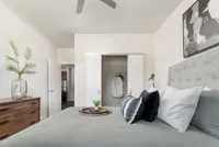 Elegant bedroom with stylish decor featuring a plush gray bed, modern artwork, and a chic wooden dresser with a glass vase.