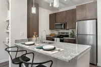 Modern kitchen with granite countertops, stainless steel appliances, and chic dining area with two stylish chairs.