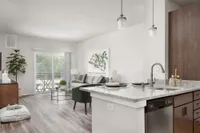 Bright, modern living room and kitchen space featuring sleek granite countertops, stylish pendant lighting, and a cozy, open layout with a view of a lush outdoor area.