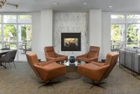Chic apartment lounge with modern leather armchairs, elegant fireplace, and floor-to-ceiling windows offering lush garden views.