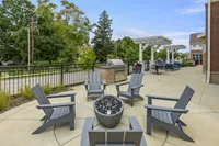 Chic outdoor patio featuring cozy Adirondack chairs around a modern fire pit, perfect for entertaining, with lush greenery and stylish pergola in the background.