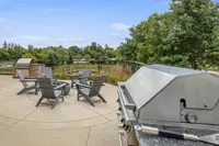 Inviting outdoor patio with modern grill, cozy seating around a fire pit, and lush, green park views.