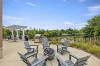 Charming outdoor patio with Adirondack chairs, fire pit, BBQ grill, and pergola, overlooking scenic greenery.