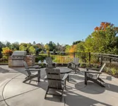 Charming outdoor patio with modern seating, barbecue area, and scenic view of lush greenery and colorful autumn trees.