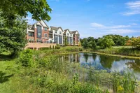 Charming apartment complex with colorful facades overlooking a serene pond and lush greenery under a clear blue sky.