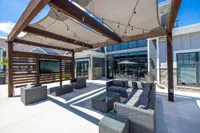 Modern outdoor lounge with stylish gray wicker seating, a pergola with integrated lighting, and contemporary decor features.