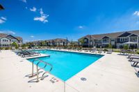 Inviting outdoor pool area with stylish lounge chairs and beautifully landscaped surroundings in a modern residential complex under a clear blue sky.