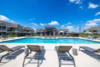 Luxurious apartment community featuring a pristine pool, stylish lounge chairs, and contemporary buildings under a vibrant blue sky.