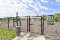 Charming fenced dog park with lush green grass and a pet waste station under a bright blue sky, perfect for pet-friendly apartment living.