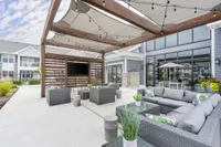 Chic outdoor lounge area with modern wicker furniture, cozy cushions, and a pergola with string lights, perfect for relaxing and social gatherings.