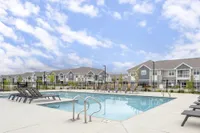 Modern apartment complex with inviting outdoor pool and sleek lounge chairs under a bright blue sky, offering a luxurious lifestyle.