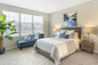 Bright and airy bedroom with elegant decor, featuring a cozy bed set, modern artwork, lush plant, and large window letting in natural light.