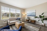 Bright and inviting living room with large windows, modern decor, and cozy seating accented by a lush indoor plant.