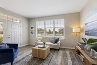 Bright and inviting living room with modern decor, featuring a cozy sofa beside large sunlit windows, blue armchair, and stylish rug, creating a warm ambiance.