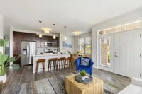 Bright open-concept living space featuring a modern kitchen with a sleek island, stylish dining area, and cozy seating, illuminated by natural light.