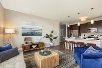 Modern living room and kitchen with open floor plan, featuring stylish furnishings, cozy seating, and elegant lighting.