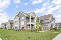 Charming two-story apartment complex with modern architecture, featuring gray siding and stone accents, surrounded by lush greenery and a well-maintained lawn under a bright blue sky.