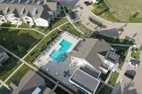 Aerial view of a modern apartment complex with a central swimming pool, surrounded by greenery and well-maintained pathways.