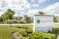 Charming exterior view of The Reserve at Kenosha, featuring lush landscaping and elegant architecture under a bright blue sky.
