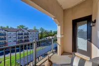 Charming apartment balcony with scenic view of modern apartment complex, lush greenery, and bright blue skies.