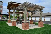 Charming outdoor pergola with brick pillars in a lush apartment community setting, perfect for relaxing and entertaining.