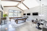 Bright and modern game room featuring a stylish pool table, sleek TVs, and cozy seating with a garden view.