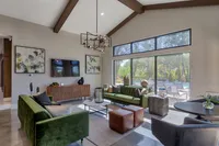 Chic living room with high ceilings, modern chandelier, and large windows overlooking a lush garden and pool.