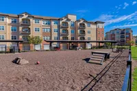 Modern apartment complex with spacious balconies, vibrant communal spaces, and a playful outdoor area under a clear blue sky.