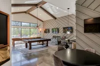 Elegant open-concept recreational area featuring a stylish pool table, modern decor, and large windows with serene garden views.
