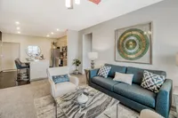 Bright and modern open-concept living space with elegant decor, featuring a cozy blue sofa, stylish armchair, and sleek kitchen with stainless steel appliances.