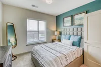 Cozy bedroom in modern apartment featuring a stylish upholstered bed, accent wall with artwork, and abundant natural light through large windows.