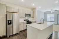 Modern kitchen with sleek stainless steel appliances, stylish wood cabinetry, and a spacious island overlooking a bright, open living area with large windows.