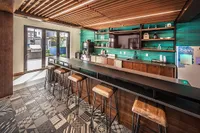 Modern communal kitchen featuring a sleek bar counter, stylish wooden stools, and vibrant teal accent wall, ideal for social gatherings.