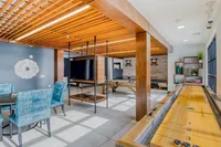 Modern apartment lounge with vibrant blue chairs, stylish wooden accents, and a recreational shuffleboard table.