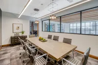 Modern conference room with sleek leather chairs, a large wooden table, and stylish pendant lighting, set against a backdrop of expansive windows and elegant decor.