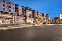 Vibrant modern apartment complex with retail spaces, featuring elegant lighting and appealing architecture in a lively urban setting.