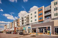 Modern apartment complex with vibrant retail spaces and chic balconies under a clear blue sky.