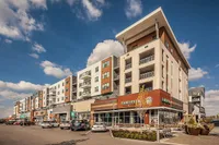 Contemporary apartment building with retail shops on ground level, featuring modern architecture and sunny outdoor spaces.