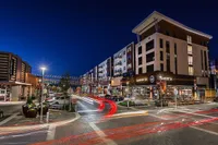 Vibrant nighttime cityscape featuring modern apartment buildings, bustling street, and lively restaurant fronts under sparkling string lights.